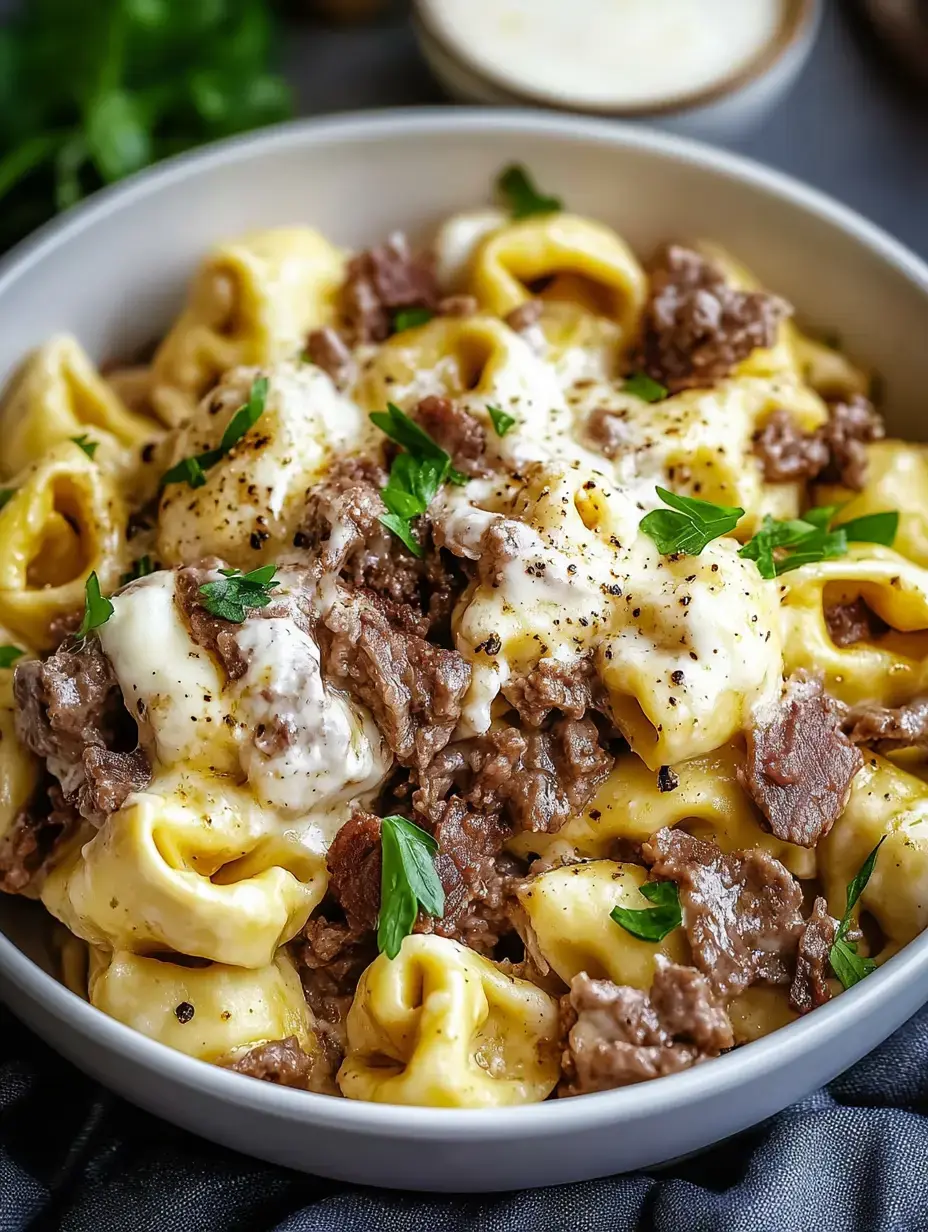 A hearty bowl of tortellini in a rich cream sauce, topped with cooked steak and parsley.