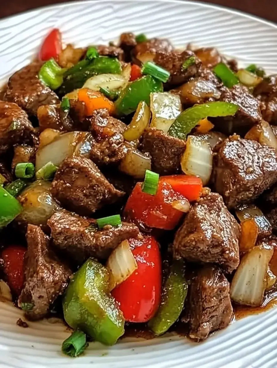 A detailed view of beef chunks cooked with colorful peppers, onions and green onions swimming in tasty sauce.