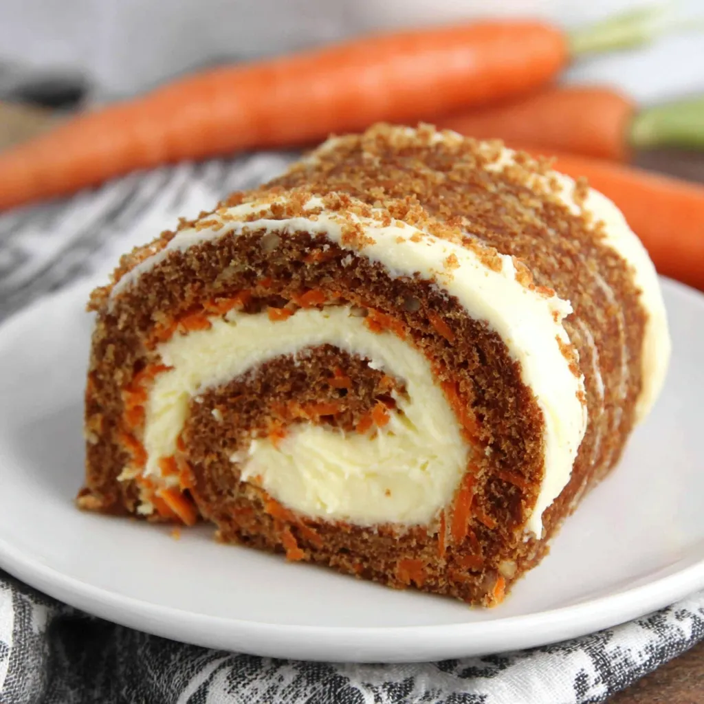 A carrot cake roll with cream cheese on a white plate.